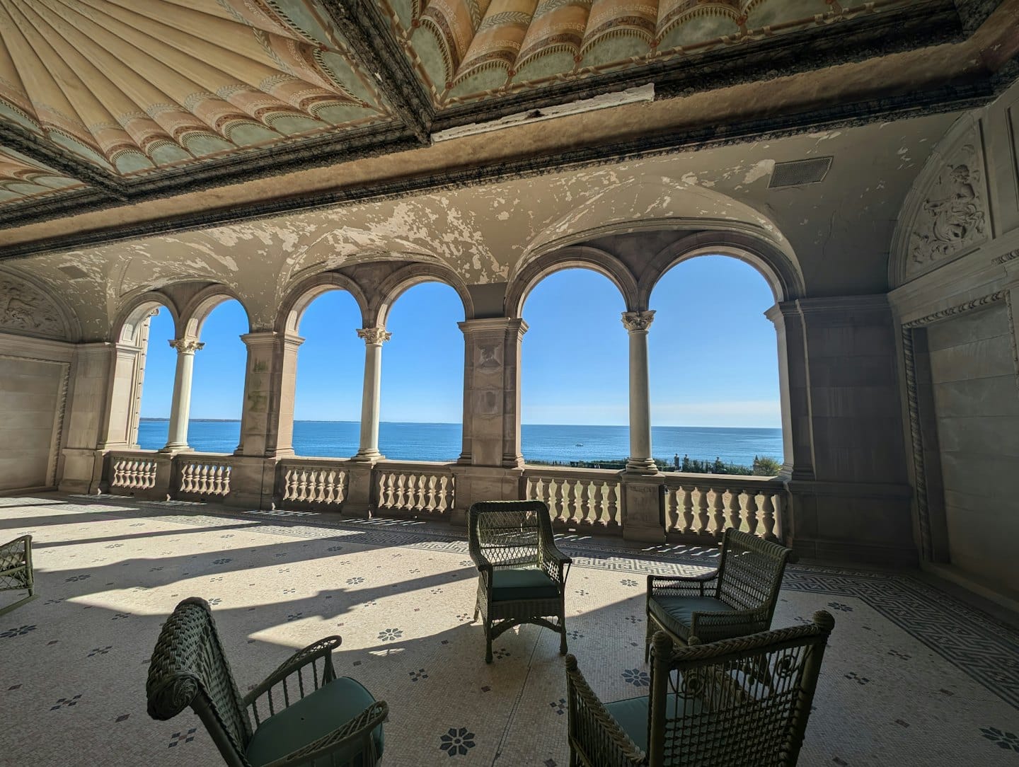 Veranda con sedie in vimini che si affaccia su un mare blu calmo.